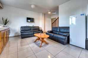 A living room with a black leather sofa, a wooden coffee table, a TV mounted on the wall, and a refrigerator. - Vétyvers - Climatisation - Terrasse (Saint-Louis)