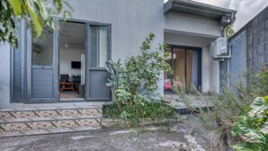 A modern building with a glass door entrance, a small patio area with plants, and a visible air conditioning unit. - Vétyvers - Climatisation - Terrasse (Saint-Louis)