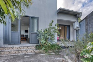 A modern building with a glass door entrance, a small patio area with plants, and a visible air conditioning unit. - Vétyvers - Climatisation - Terrasse (Saint-Louis)