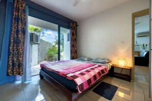 A bedroom with a bed, a bedside table with a lamp, a window with curtains, and a view of the outside. - Vétyvers - Climatisation - Terrasse (Saint-Louis)