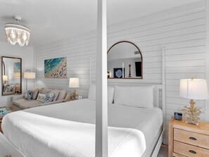 A hotel room with a large bed, a sofa, a nightstand with a lamp, a mirror, and a painting on the wall. - Bahia 4122 (Miramar Beach)