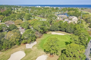 Ein Luftbild eines Golfplatzes mit Sandbunkern, Bäumen und Wohnhäusern im Hintergrund.