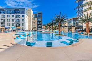 A hotel pool area with multiple levels of buildings, palm trees, and lounge chairs. - The Golden Hour Loft, a 2bed 2bath apartment in the heart of Addison. (Addison)