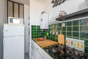 Une cuisine compacte avec un réfrigérateur blanc, un four à micro-ondes, un évier doté d’une planche à découper en bois et une cuisinière à gaz.