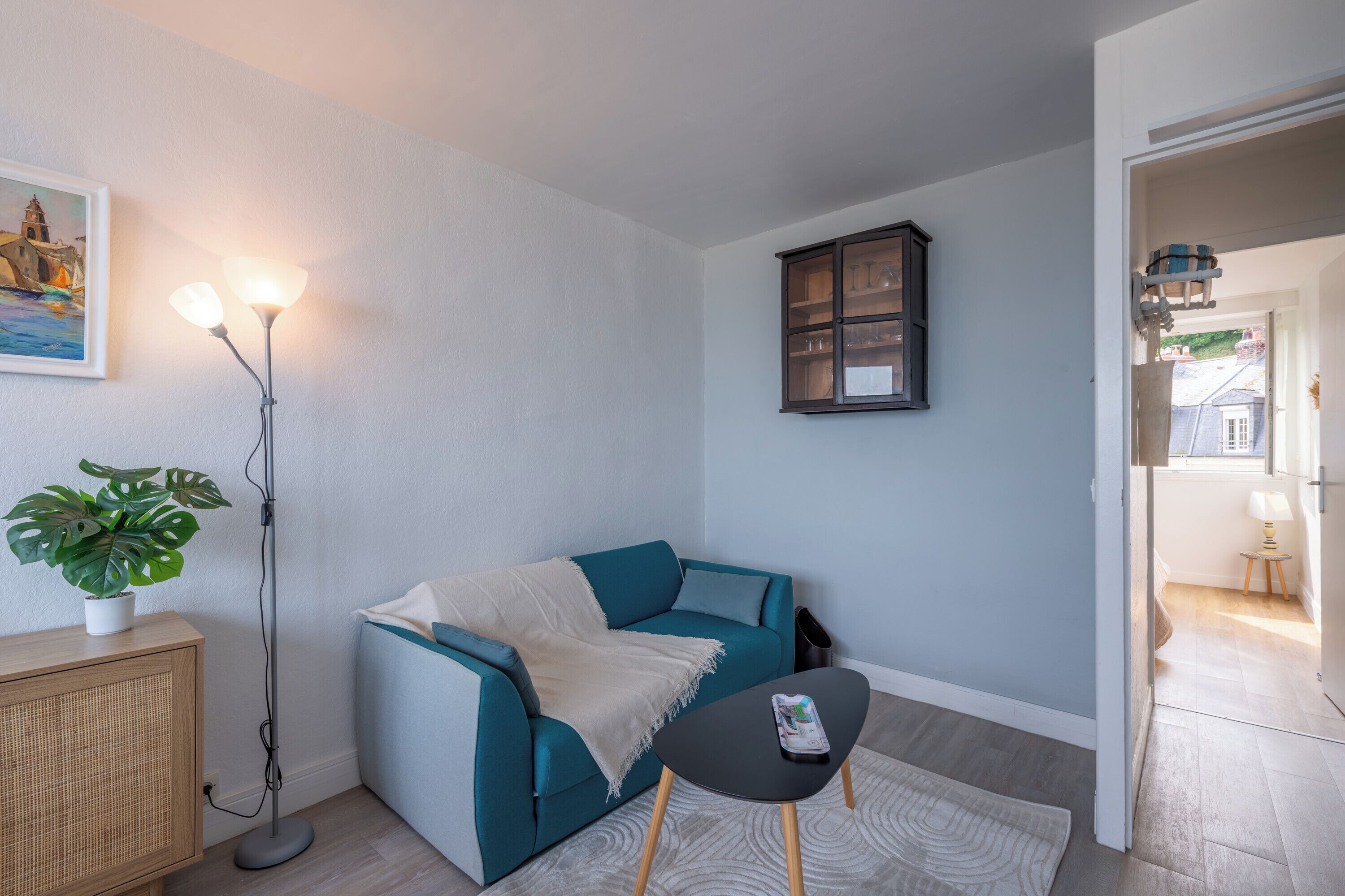 Ein modernes Wohnzimmer mit einem türkisfarbenen Sofa, einem kleinen schwarzen Tisch und einer Stehlampe.