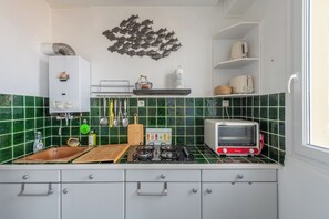 A kitchen with green tiles, a gas stove, a toaster, and a wall-mounted shelf with kitchen items. - Le Relai de la Marée -Plage -Petfriendly (Le Tréport)