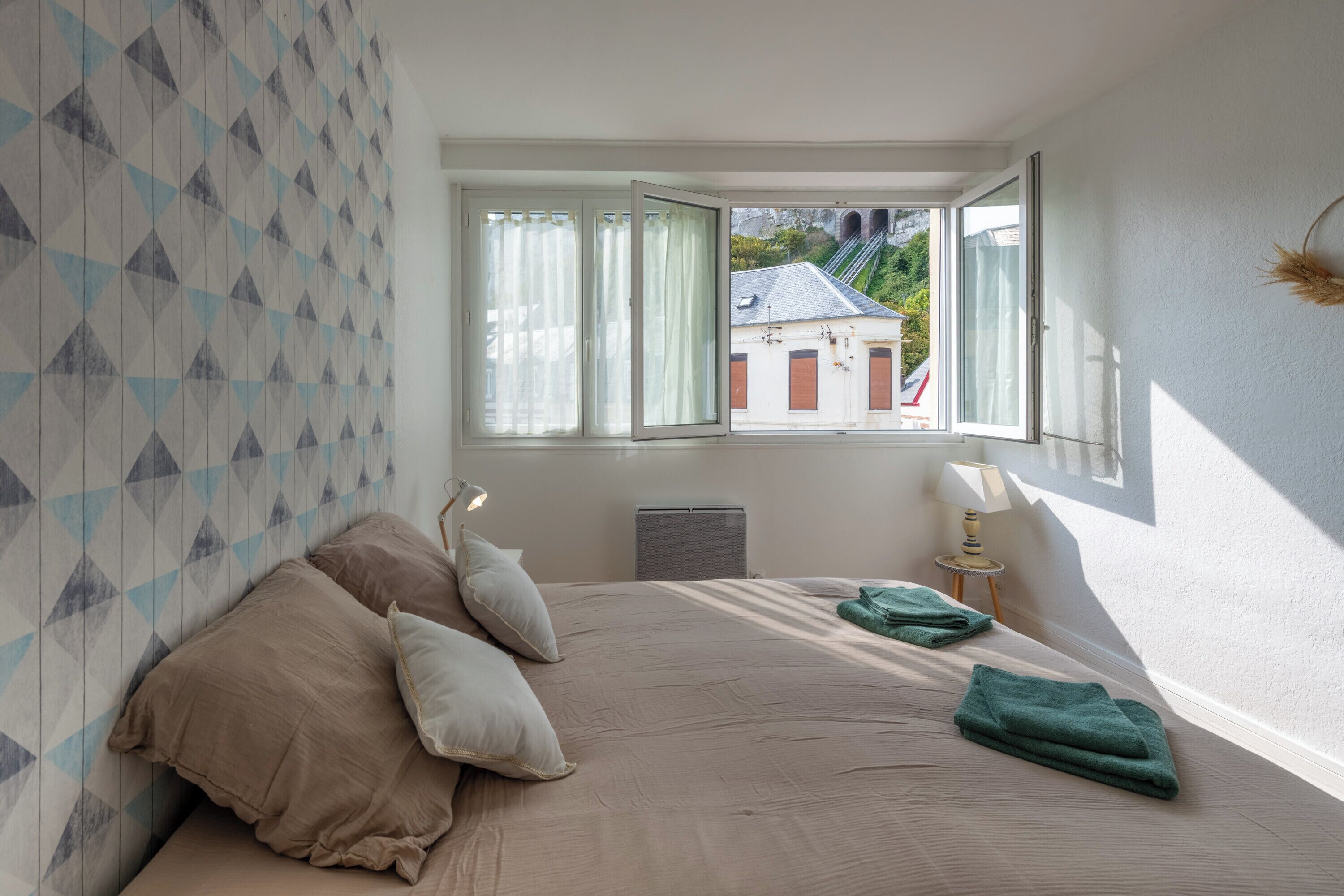 Ein Schlafzimmer mit einem großen Bett, einem Heizkörper, einem Fenster mit Vorhängen und Blick auf Gebäude.