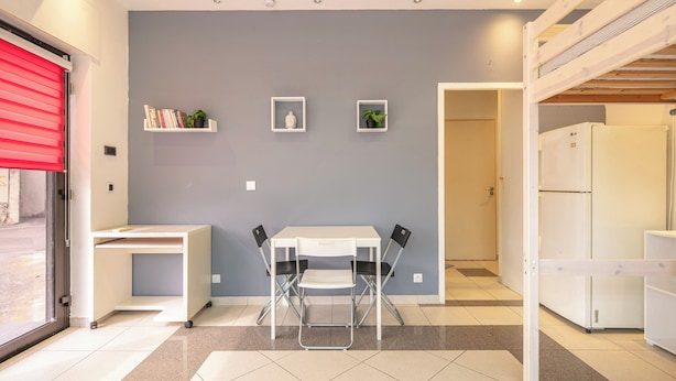 A modern kitchen with a white refrigerator, a dining table with chairs, and a grey wall with two small shelves. - Le Local - Climatisation - Petfriendly (Saint-Martin-d'Hères)