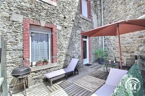 Eine Terrasse mit Grill, Liegestühlen und einem Tisch mit einer Flasche.
