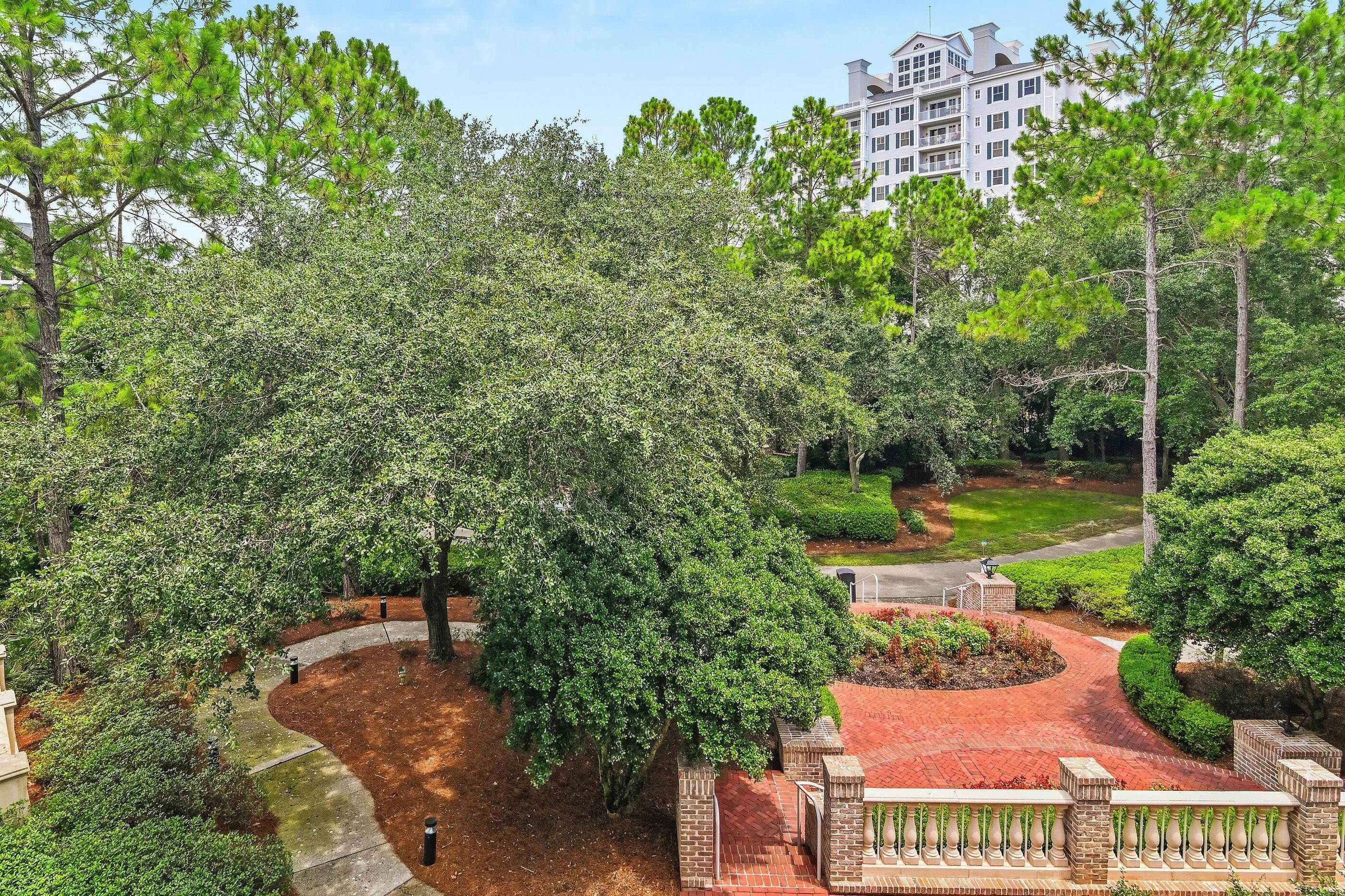A landscaped garden with a central tree, a brick pathway, and a building in the background.