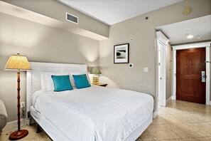 Un dormitorio con una cama grande, una lámpara de noche, un cuadro en la pared y una puerta a la derecha.