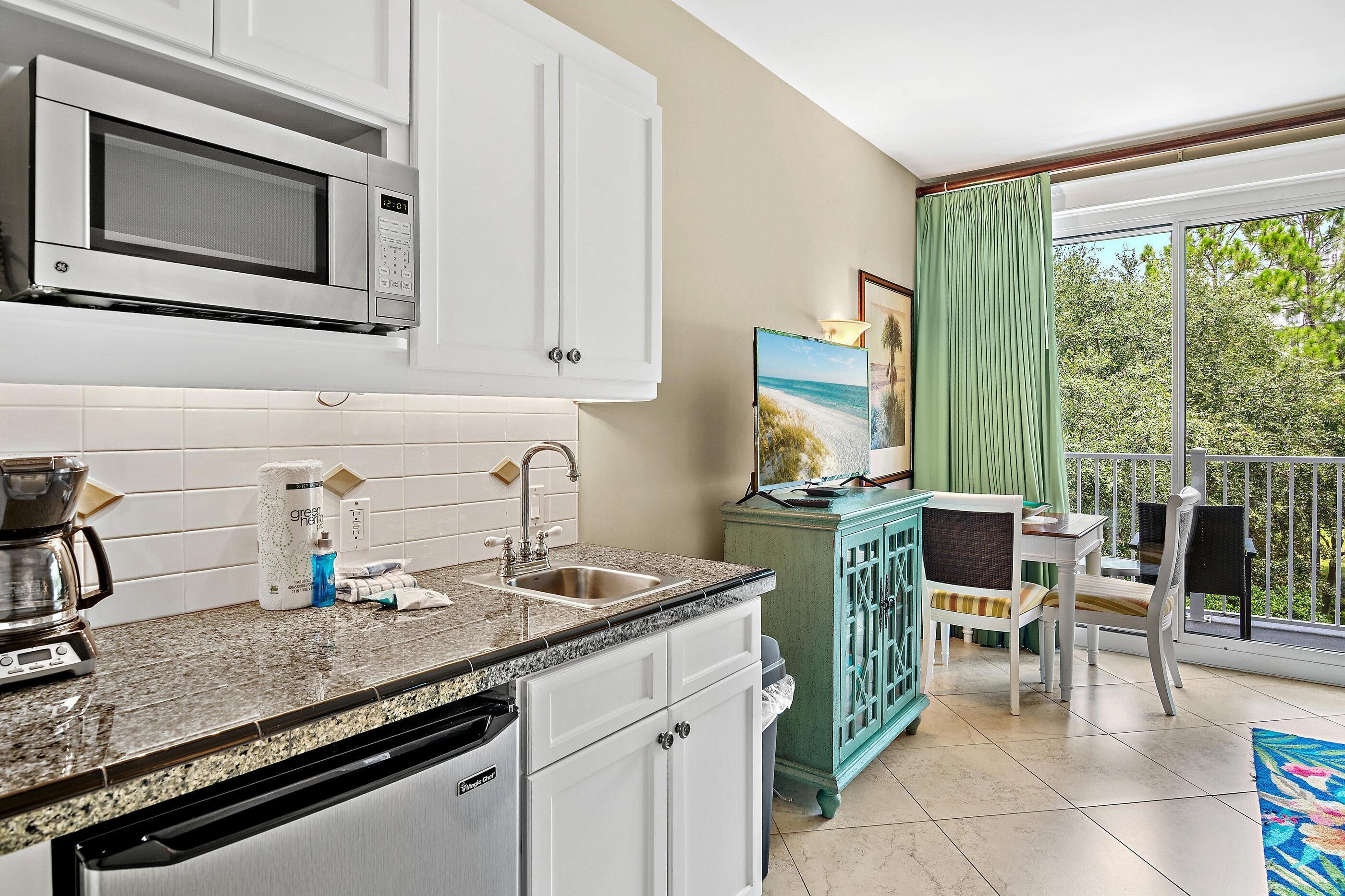 A kitchen with a microwave, sink, and dishwasher. There is a dining area with a table and chairs. A painting is visible on the wall.