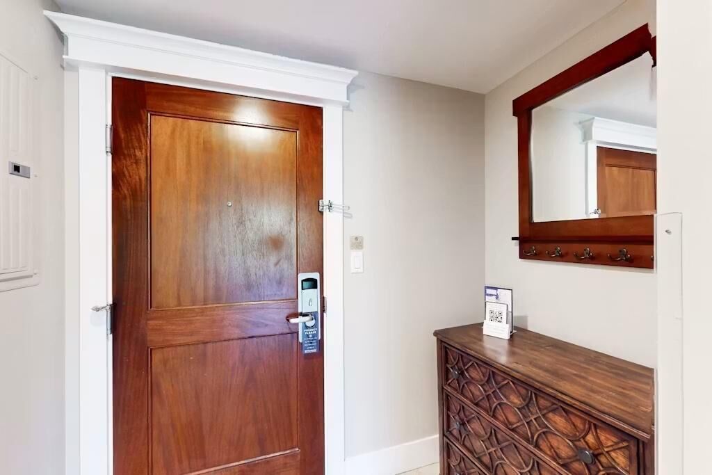 Una puerta de madera con cerradura electrónica, un aparador de madera con cajones y un espejo sobre el aparador.