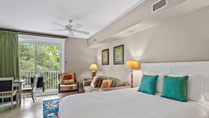 A hotel room with a bed, two bedside lamps, a ceiling fan, a sofa, a chair, a small table, and a balcony with a view of greenery. - Lasata 3315 (Miramar Beach)