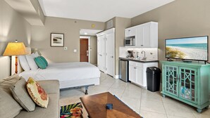 A compact living space with a bed, a sofa, a television, a kitchenette, and a view of the beach. - Lasata 3315 (Miramar Beach)