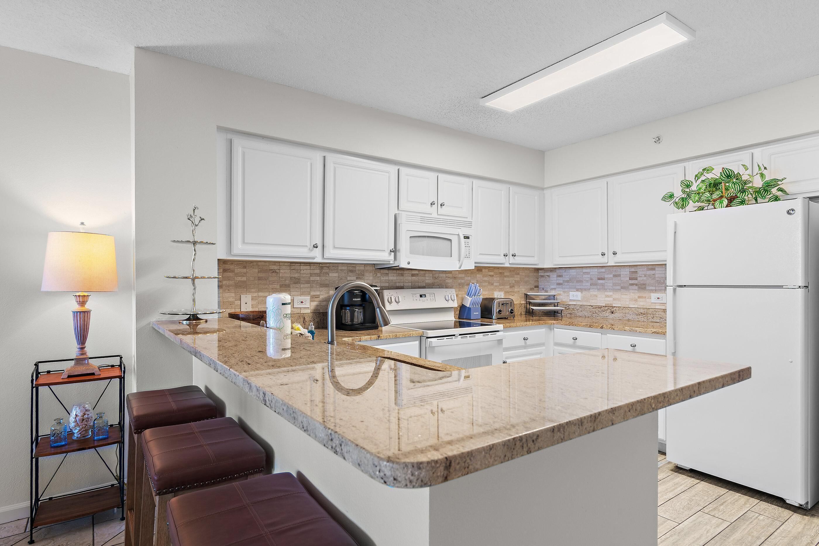 A modern kitchen with white cabinets, a granite countertop, a built-in microwave, a coffee maker, and a refrigerator.