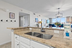 A modern kitchen with granite countertops, stainless steel sink, and white cabinetry. - Pelican Beach Terrace 903 (Destin)