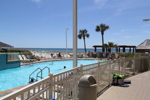 Ein Poolbereich mit Liegestühlen und Sonnenschirmen, mit Blick auf das klare Meer, und eine Holzhütte.