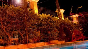 A swimming pool with clear water, surrounded by a wooden deck and a hedge. - Chalé Jardim Itália (Tiangua)