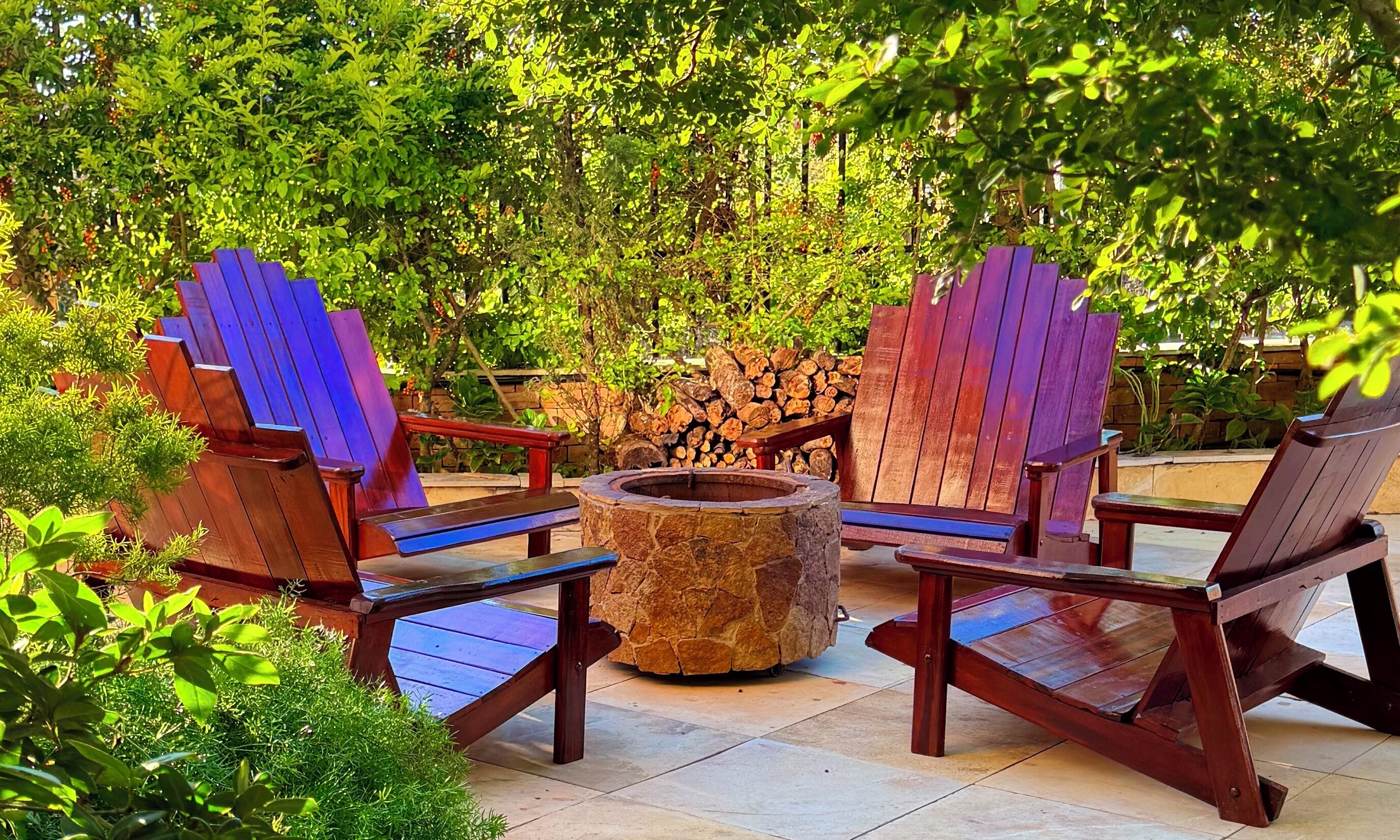 A patio with Adirondack chairs, a stone fire pit, and a stack of firewood.