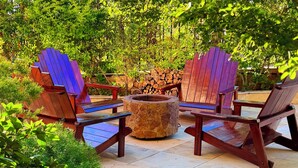 A patio with Adirondack chairs, a stone fire pit, and a stack of firewood. - Chalé Jardim Itália (Tiangua)