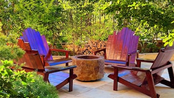 A patio with Adirondack chairs, a stone fire pit, and a stack of firewood.