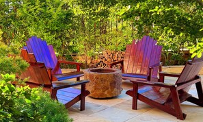 A patio with Adirondack chairs, a stone fire pit, and a stack of firewood. - Chalé Jardim Itália (Tiangua)