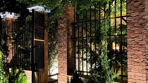 A gated entrance with brick pillars and metal bars, surrounded by lush greenery and a well-lit pathway. - Chalé Jardim Itália (Tiangua)