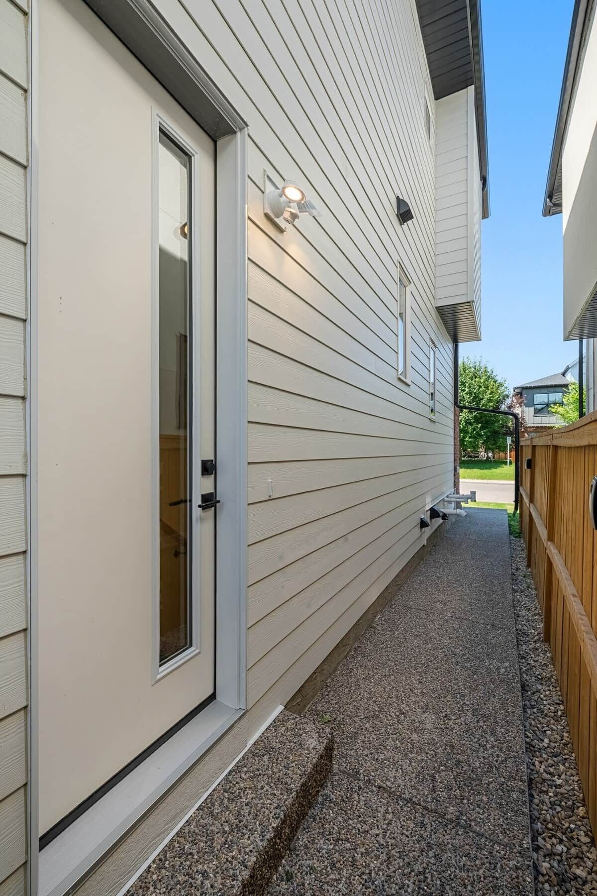 A residential building with a door, a small window, and a pathway leading to a wooden fence.