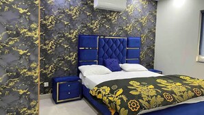 Un dormitorio con cabecera azul, cama con ropa de cama blanca y azul, y una colcha estampada con motivos florales.