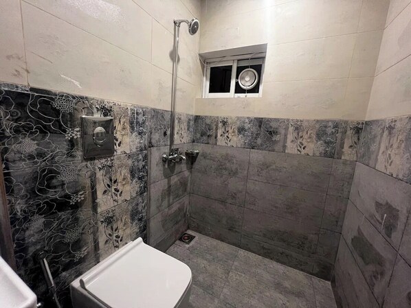 A bathroom with a shower, toilet, and a small window.