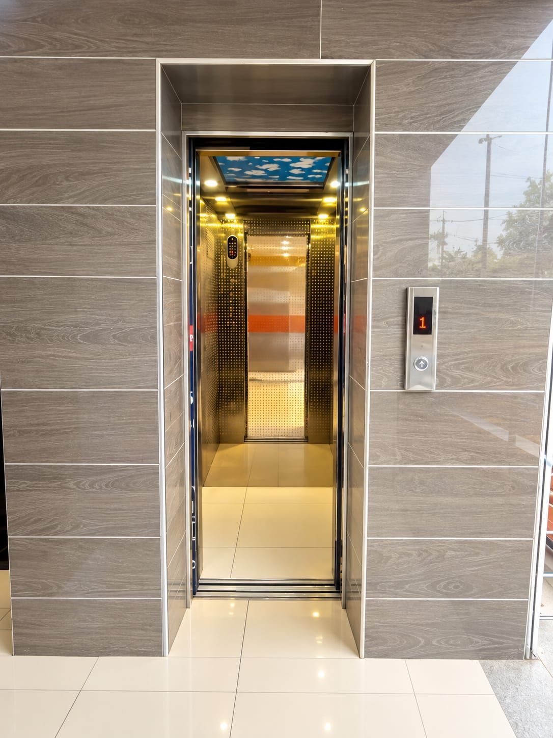 An elevator with a digital display showing the number 1, a control panel, and a ceiling with a blue sky and clouds design.