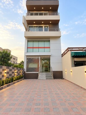 A modern building with a flat roof, a central entrance with a glass door, and a staircase leading to the entrance.