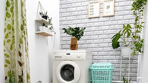 Un área de lavandería con lavadora, una planta colgante, una planta en maceta y una cesta de ropa.