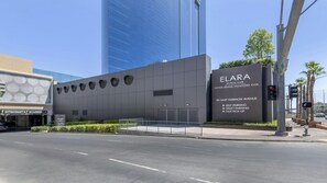 Ein modernes Gebäude mit einem Schild für den Elara Hilton Club, das Selbstparken, Valet-Parken und Taxifahrt-Service anzeigt.