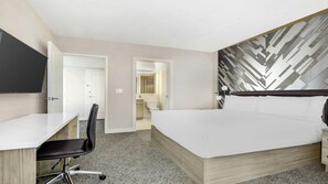 Ein Hotelzimmer mit Bett, Schreibtisch, Stuhl und einem durch eine geöffnete Tür einsehbarer Badezimmer.