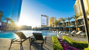 Ein Hotelpoolbereich mit Liegestühlen, einer großen Werbetafel und hohen Gebäuden im Hintergrund.
