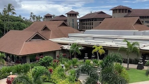 Ein Resort mit mehreren Gebäuden, darunter ein zentrales Gebäude mit flachem Dach und kleinere Gebäude mit Satteldächern. Freiluft-Sitzbereiche mit Tischen und Stühlen sind von üppiger Vegetation und Palmen umgeben.