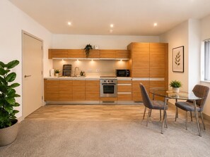 A modern kitchen with wooden cabinets, a microwave, a stove, and a dining area with two chairs. - 2 bedroom apartment with en-suite bathroomin the heart of the city (Manchester)