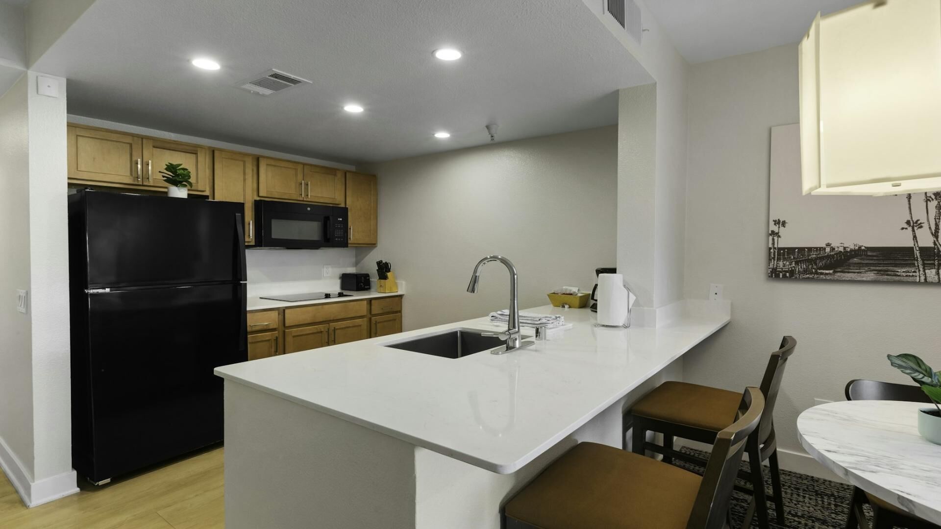 A modern kitchen with a black refrigerator, a microwave, and a sink. There is a dining area with a table and chairs.
