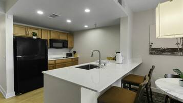 A modern kitchen with a black refrigerator, a microwave, and a sink. There is a dining area with a table and chairs.