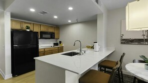 A modern kitchen with a black refrigerator, a microwave, and a sink. There is a dining area with a table and chairs.