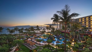 Ein Resort mit Poolbereich, Palmen und Blick auf das Meer im Abendlicht.