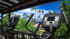 Appareils de musculation dotés d’un écran numérique, placés devant un décor de verdure luxuriante et d’un ciel bleu dégagé.