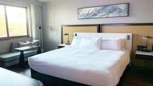 Een hotelkamer met een groot bed, een zithoekje, een bureau en een kunstwerk aan de muur.