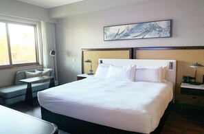 Ein Hotelzimmer mit einem großen Bett, einer kleinen Sitzecke, einem Schreibtisch und einem Wandbild.