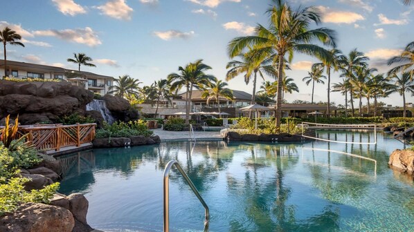 Ein Resort-Pool mit Wasserfall, Palmen und Blick auf die Resort-Gebäude.