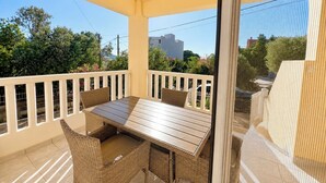 Ein Balkon mit Holztisch und Korbstühlen, mit Blick auf einen Garten und Gebäude.