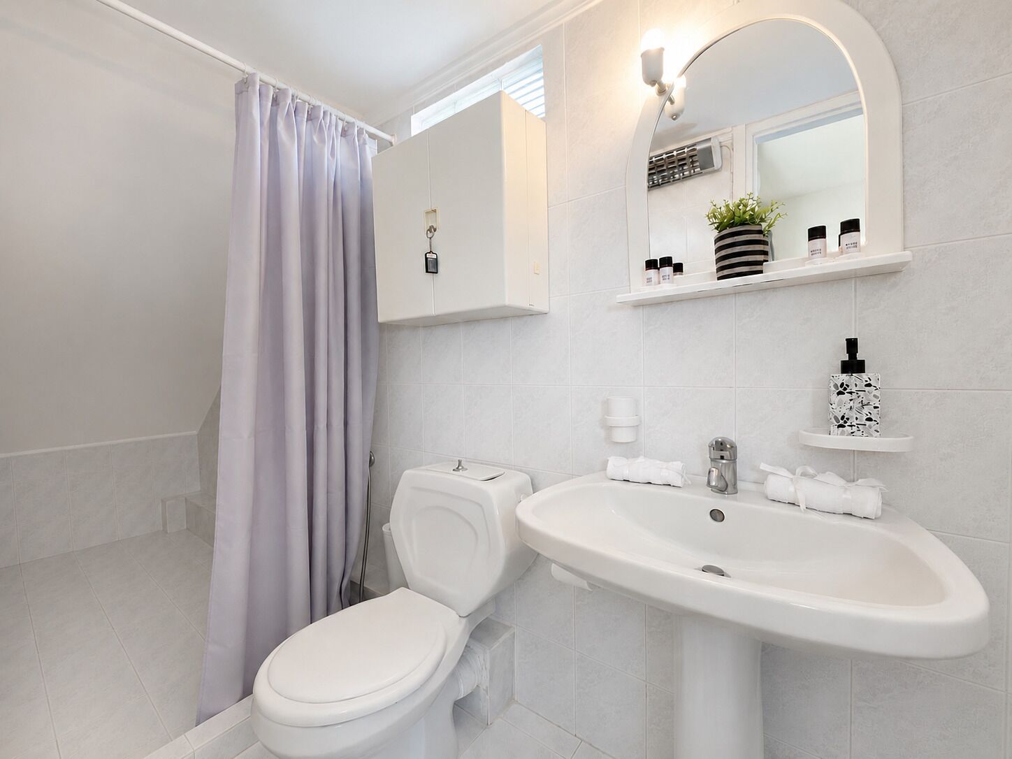 Un baño con inodoro, lavamanos, cortina de ducha y espejo.