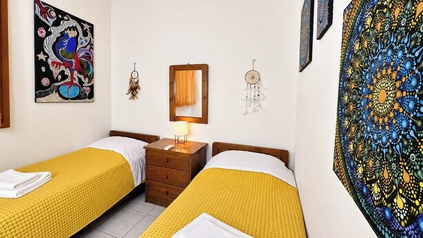 A hotel room with two beds, a nightstand, a lamp, and wall art.